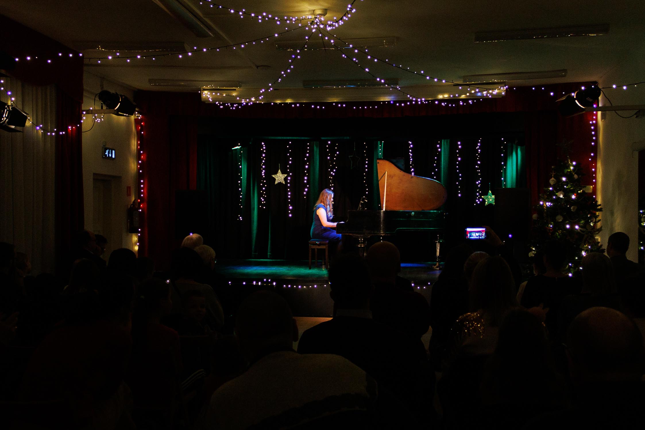 kolorowa scena, dziewczyna gra na fortepianie, w tle oświetlona scena, scena udekorowana świątecznie, szeroki kadr, widać publiczność