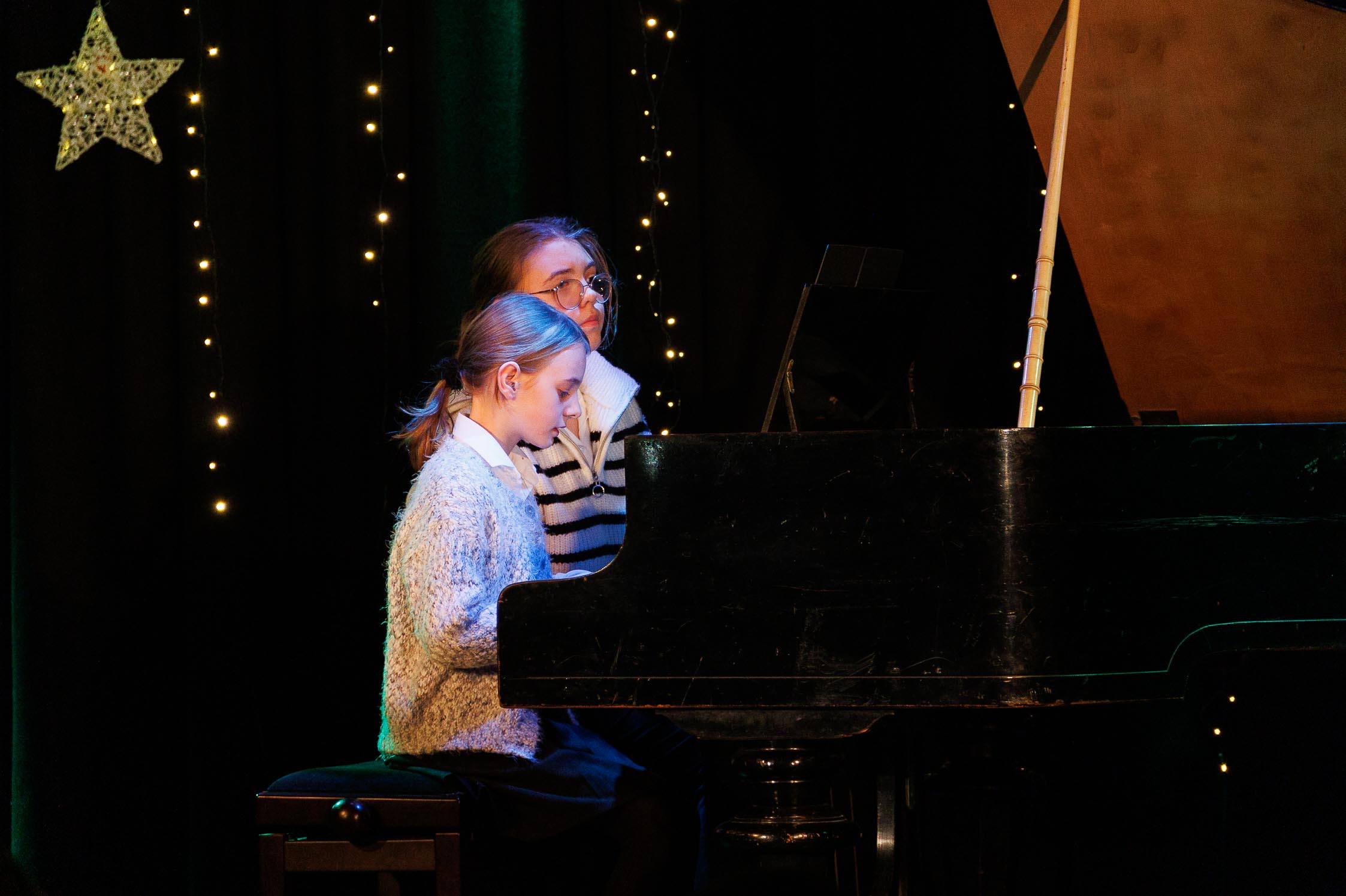 dwie dziewczynki grają na fortepianie, w tle gwiazda betlejemska, na twarzach widać skupienie