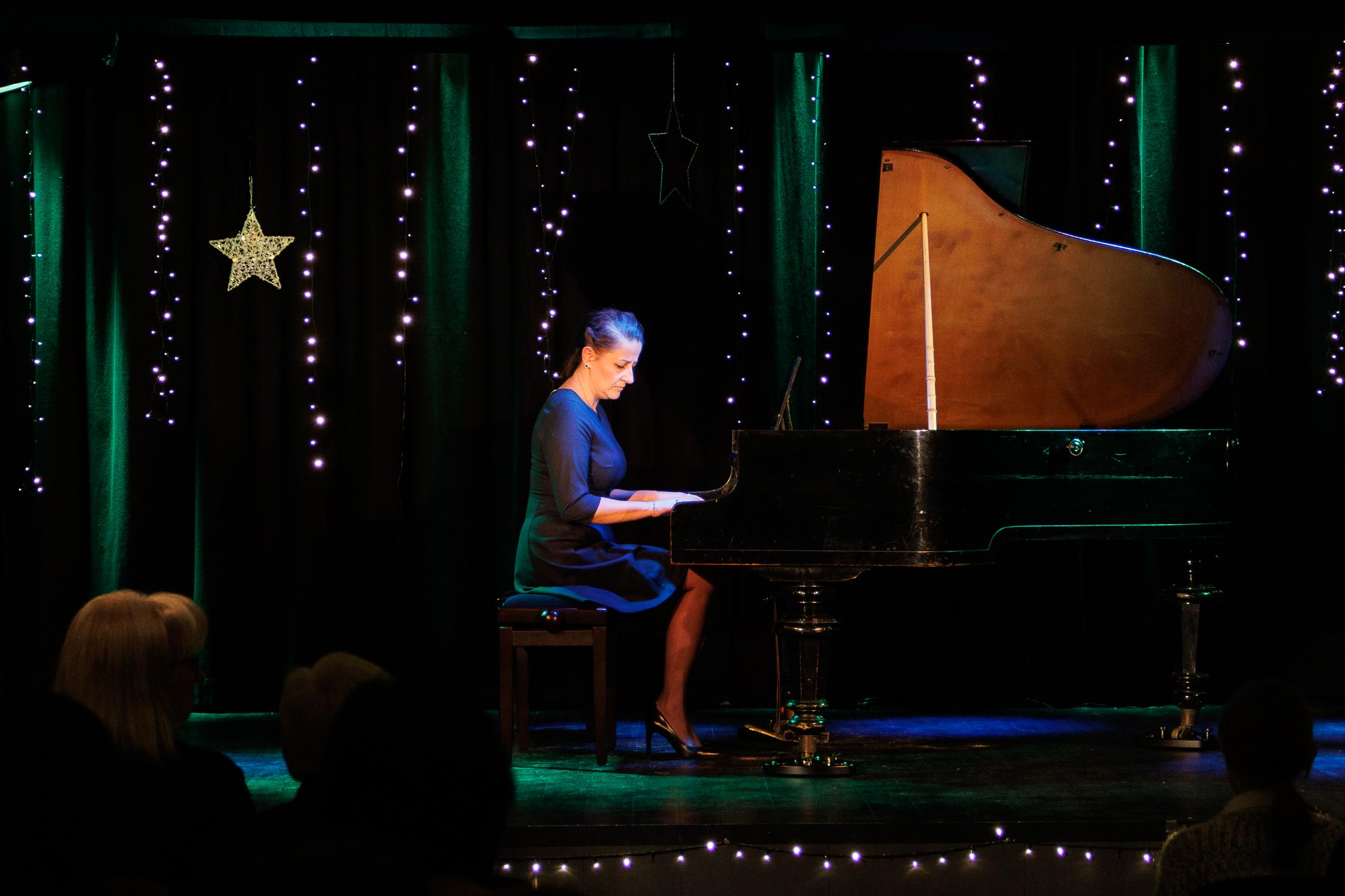 kobieta w średnim wieku gra na fortepianie, w tle kolorowa scena - dużo kolorowych światełek 