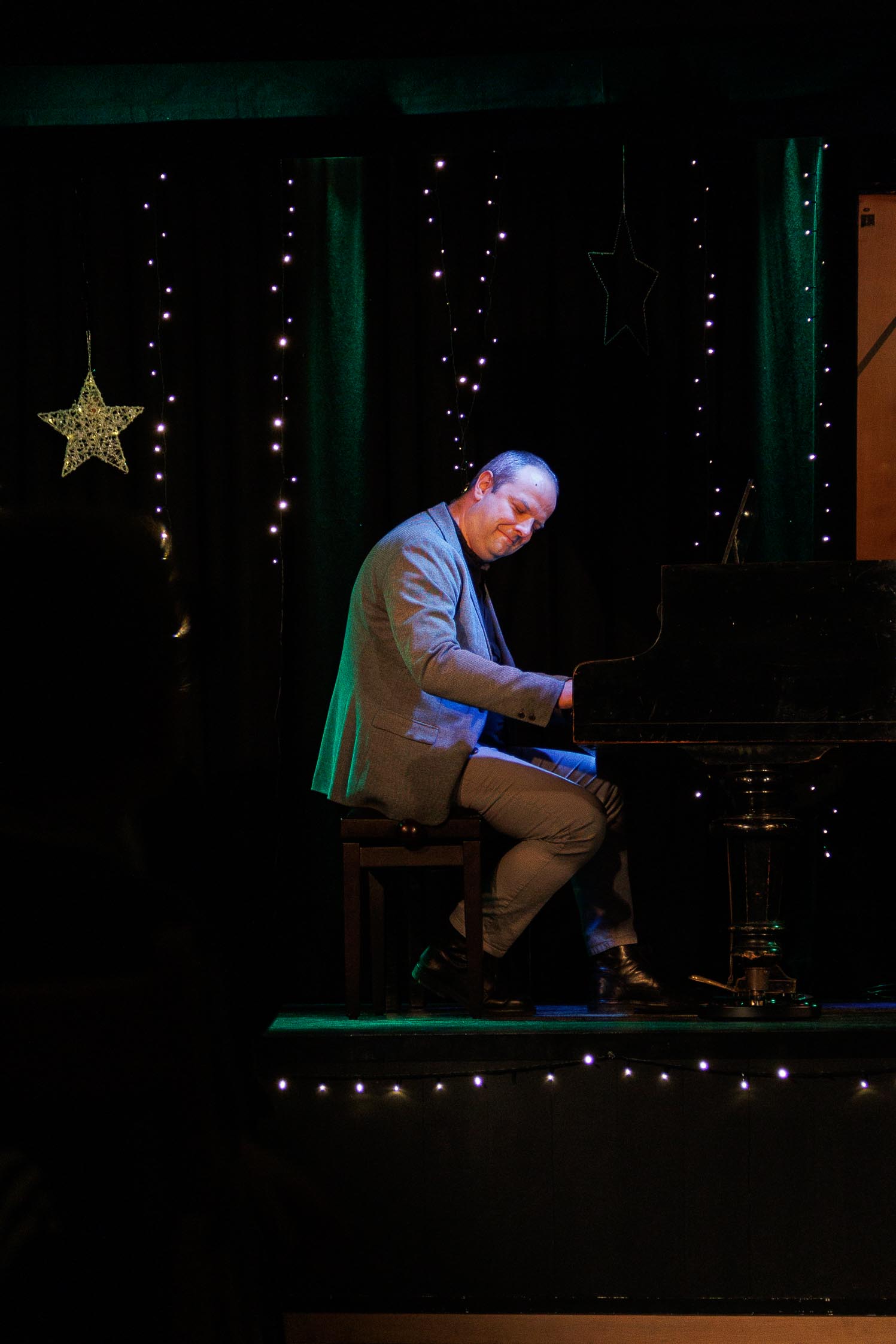mężczyzna w średnim wieku, z przejęciem gra na fortepianie, ubrany jest w garnitur, w tle scena
