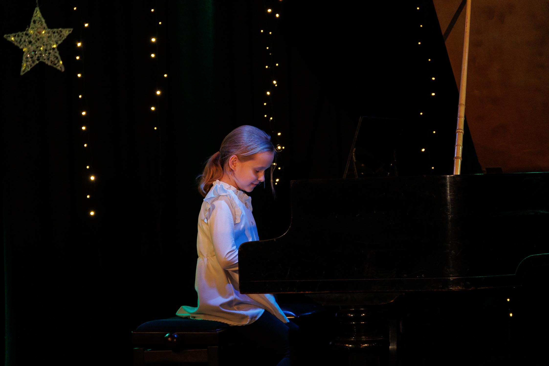 dziewczynka siedzi przy fortepianie i się uśmiecha, w tle świąteczna dekoracja