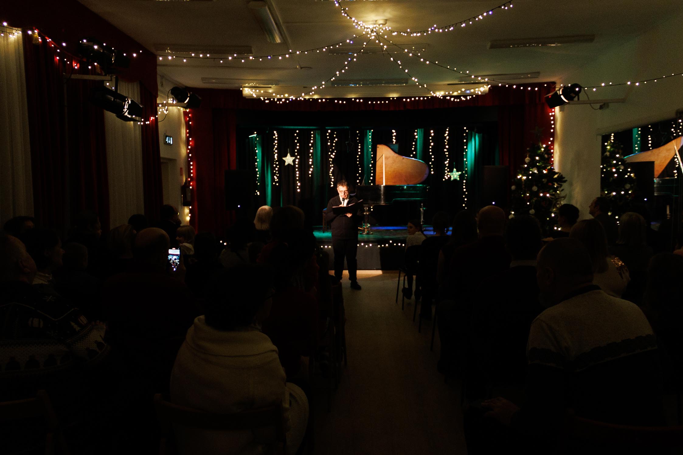 widok na całą salę widowiskową, przyozdobioną świątecznie, w centrum mężczyzna który zapowiada następny utwór